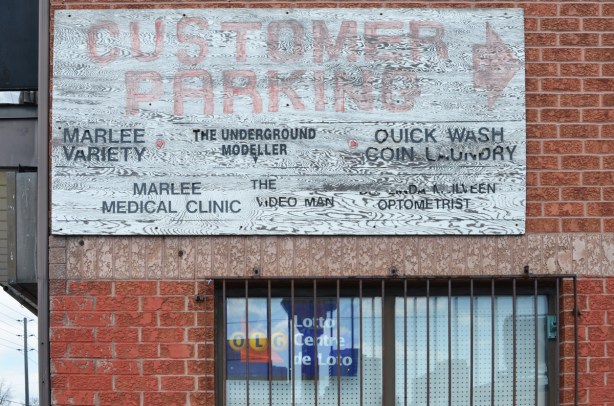 old sign on the side of brick store that says customer parking in faded red letters and then it lists the stores in that plaza