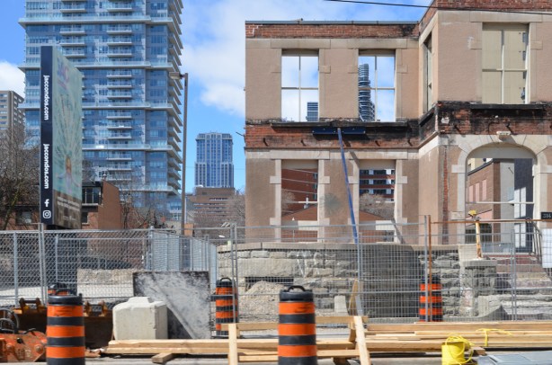 partial demolition of an old house on Jarvis street, facade is left standing, no glass in the windows, can see other high rise downtown buildings through the window holes