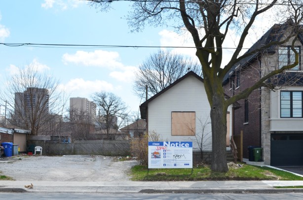 blue and white development notice in front of a small white house and a vacant lot, to be replcaed with 8 storey condo