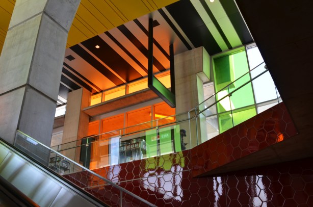 escalator and levels of Finch west subway station, lots of coloured panes of glass, greens, and oranges,