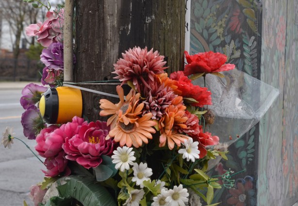 a bunch of fake flowers tied to a pole at an intersection, beside a metal box that has been painted with flowers 