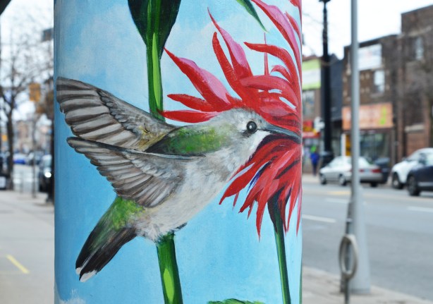 street art of a hummingbird on a pillar, with red flower 
