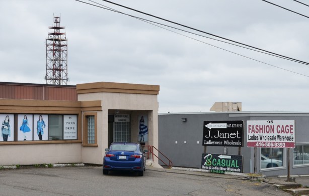 two low rise warehouses, one is Janet Ladieswear with faded pictures of women's clothing in the window, sign beside it for Fashion Cage ladies clothing wholesale, 