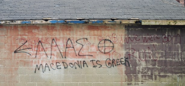 Words scrawled on the side of a concrete block garage in an alley that say Macedonia is Greek 