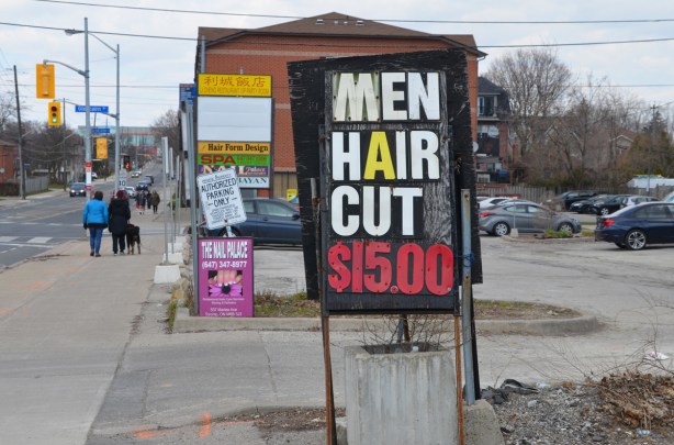 a sign that says men hair cut fifteen dollars, beside the sidewalk in front of a plaza 