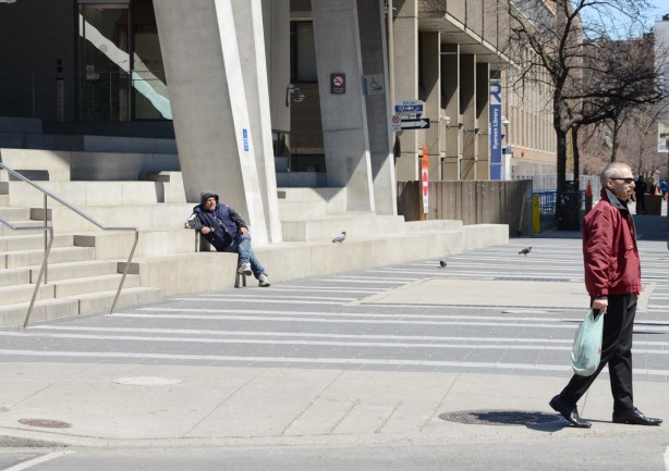 a man sits on the stairs in front of the Ryerson Student Union building while another man walks past 