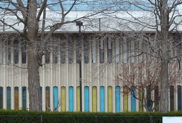 two trees in front of a concrete building with lots of narrow vertical windows