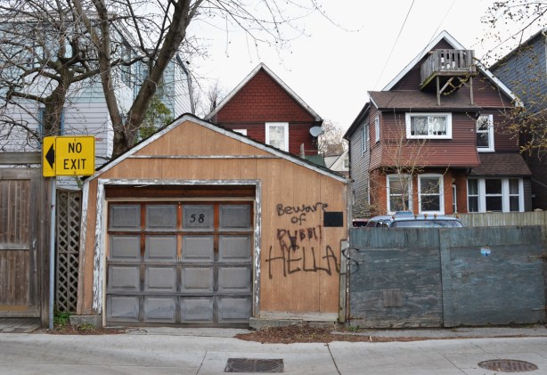 backs of houses and a garage in an alley, graffiti on garage says beware of rabbits