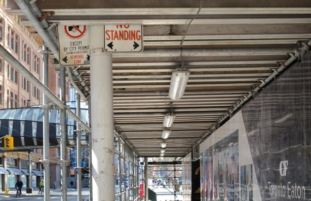 street signs now partially obscured by covering over sidewalk at construction site 