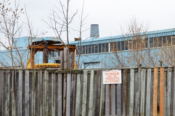 a fence with a no trespassing sign, with industrical building behind