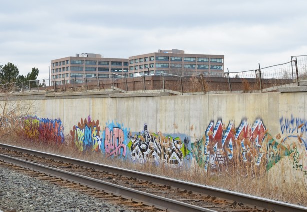 graffiti, tags, along the concrete embankment beside the CPR tracks, apartment buldings can be seen over the wall
