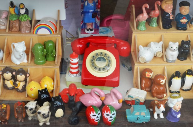 looking in a store window, bright red rotary phone and a display of different types of salt and pepper shakers in differernt shapes - flamingoes, monkeys,