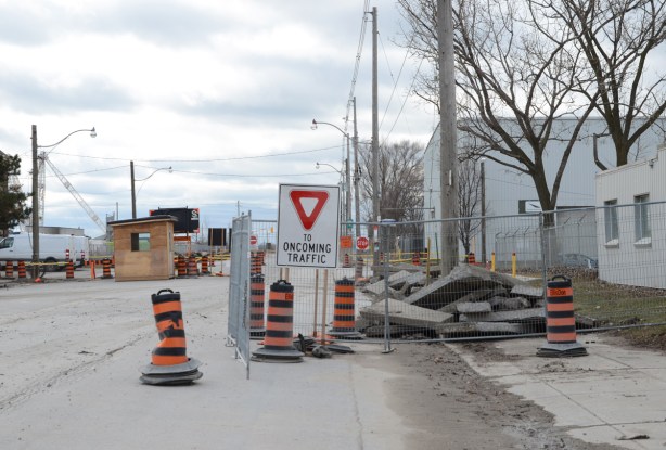 Commissioners street in the port lands, road closed, yield sign on road yield to oncoming traffic, black and orange traffic cones, a plywood booth for security guard to sit in, 