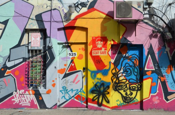 wall and doors to numbers 533 and 535 covered with street art including an urabn ninja squadron character with a face mask on with the words stay safe 