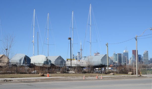 a line of large sail boats in storage, on land, covered with tarps, masts in the air, no sails, 