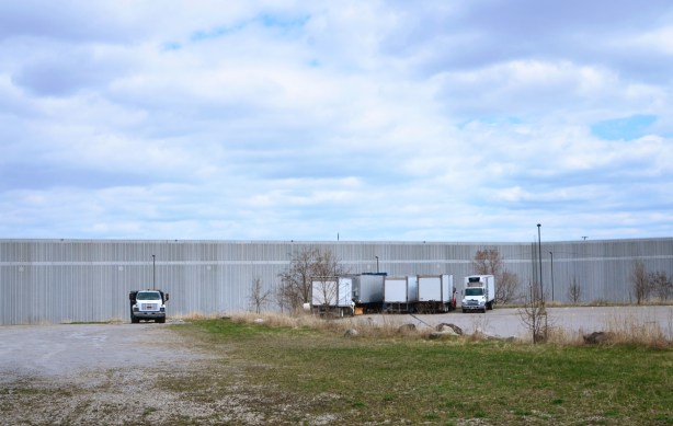 trucks parked beside a long low grey building, in the distance. in front is a vacant lot 