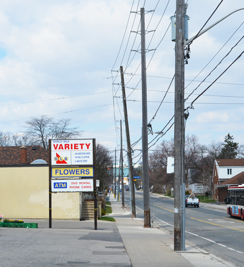 sidewalk lined with wood utility poles with wires, a sign for Variety store with store that sells DVDs 