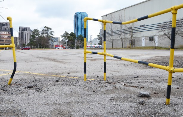 bent metal pipes as a railing, painted in yellow and black, empty parking lot beyond with a couple a buildings in the background 