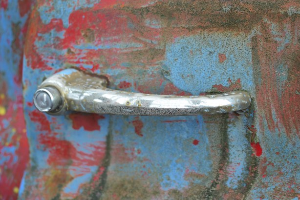 junked, old cars, McLeans Auto Wreckers, corroded chrome handle of a door, pink and light blue with rust spots
