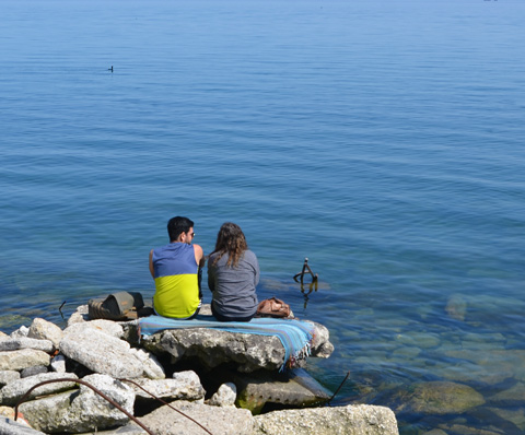a couple sit on a rock by Lake Ontario