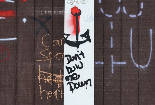 graffiti on a brown garage door, picture of an anchor along with words don't hold me down 