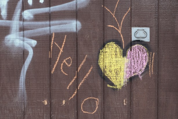 graffiti on a brown garage door, chalk heart in pink and yellow with orange word hello written beside it 