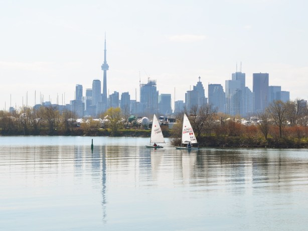 two sailboats exit the marina harbour and pass by the Toronto skyline (seen from the east)