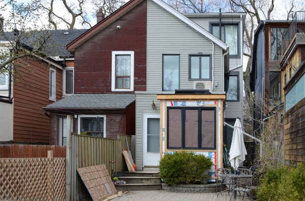 back of a semi divided house, older asphalt shingles on exterior of the one on the left while on right has been renovated in light grey with new large window on ground floor 