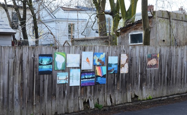paintings on a wood fence, with backs of houses in the background