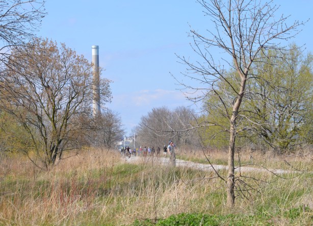 tall smokestack in the distance, a park in the foreground, with a bike path and cyclists running through the park, early spring 