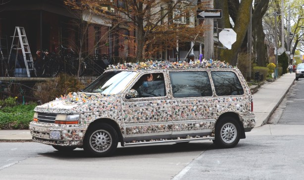 side of van covered with shells and small toys, driver is waving from partially lowered window 