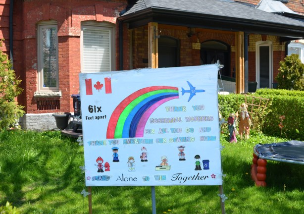 home made sign on the front yard of a house with a Canadian flag, a rainbow, and an airplane 