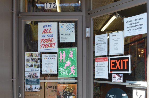 a large number of notices and posters on a glass door and window, including, we're all in this together,