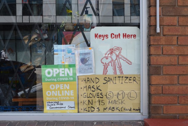 signs and posters in the window of a convenience store, Sun Milk, advertising hand sanitizer and kids face masks for sale, also keys cut,
