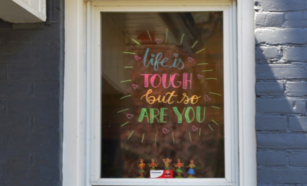 painted sign in the window of a house that says Life is tough but so are you