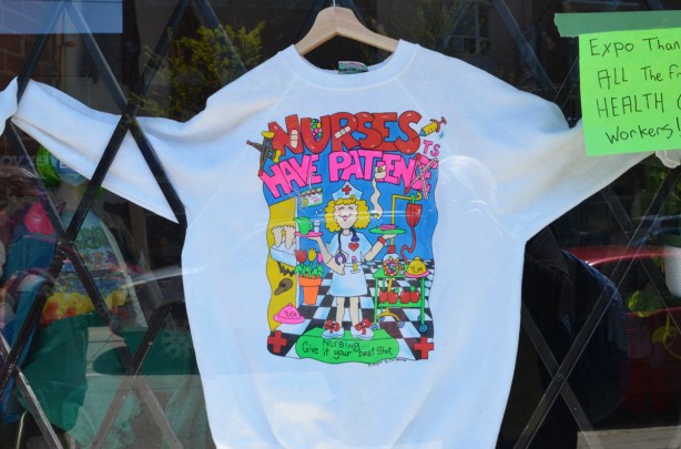 a white sweatshirt in the window of a store, that says Nurses have patience 