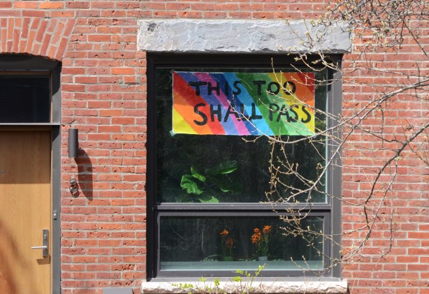 sign in window of house, rainbow with words this too shall pass 