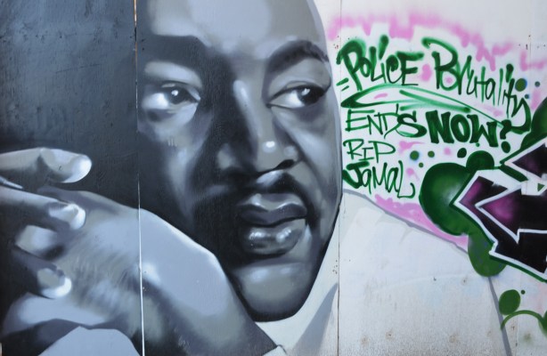 A portrait of Martin Luther King Jr. painted in a mural, along with words in green paint that say Police brutality ends R I P Jamal 