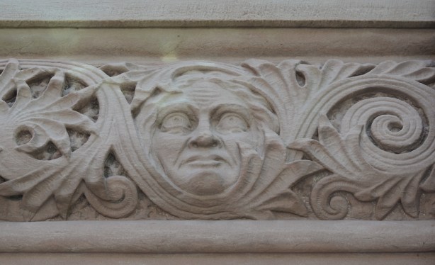 in a carved frieze on the exterior of parliament buildings, a face with blank eyes 
