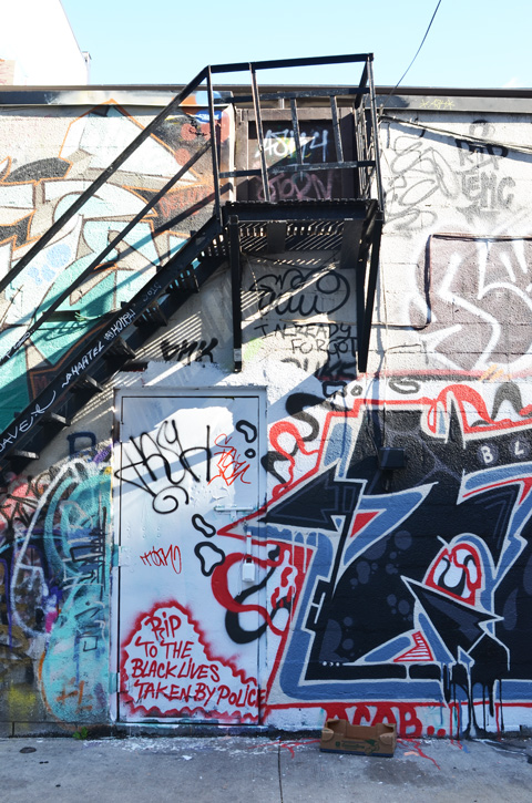 wall in Graffiti Alley, back of two storey building with exterior metal stairs, wall is covered with graffiti including words R I P to the black lives taken by police