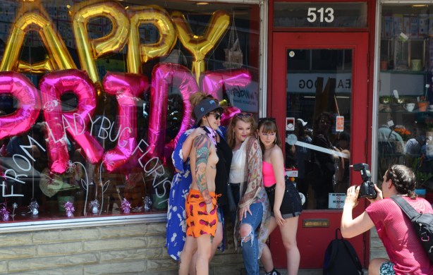 young people posing for pictures outside store with happy pride balloons in the window