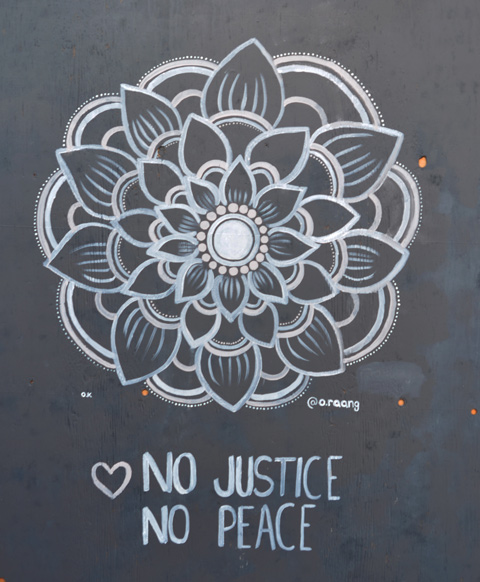 A circular design in light grey on black in a flower shape with words under that say no justice no peace 