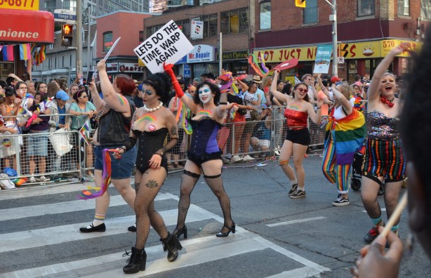 Rocky Horror theme group at pride parade with sign that says let's do the time warp again 