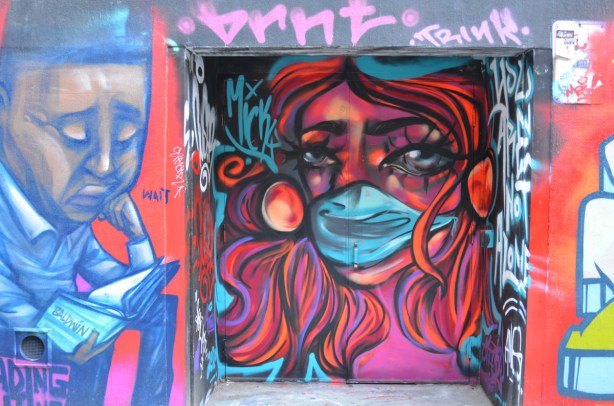 mural of woman in bright colours, reds and pinks, wearing a blue mask, tribute to health care workers.