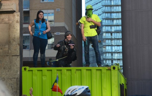 3 people on top of green container watching pride parade 
