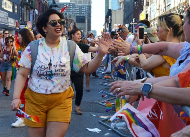 woman in Waterloo Engineering society t-shirt high fives with crowd watching pride parade 