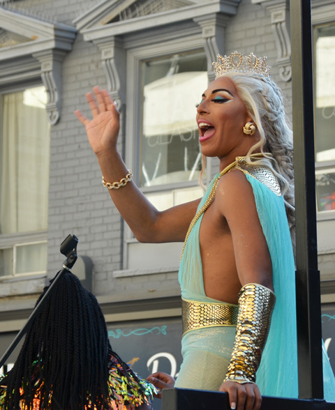 on float at pride, in long turquoise dress and platinum blond hair 