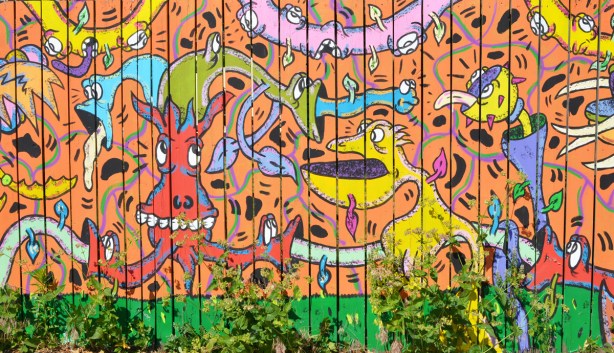 part of an Al Runt mural on a fence, orange background with lots of his typical characters in bright colours 