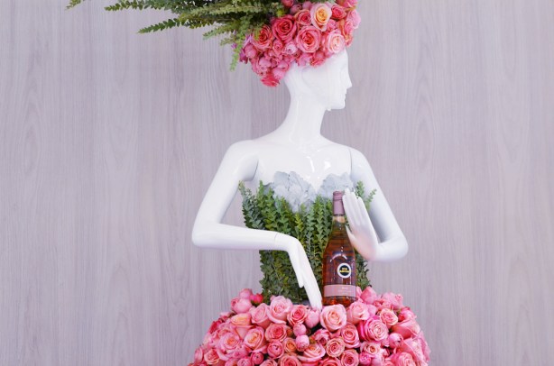 mannequin in green and pink dress and pink hat, pinks are made of roses and she is holding a bottle of rose wine from the LCBO