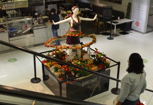 a mannequin decorated with flowers stands at the bottom of an escalator at the Manu Life center, as part of Fleurs de Villes project